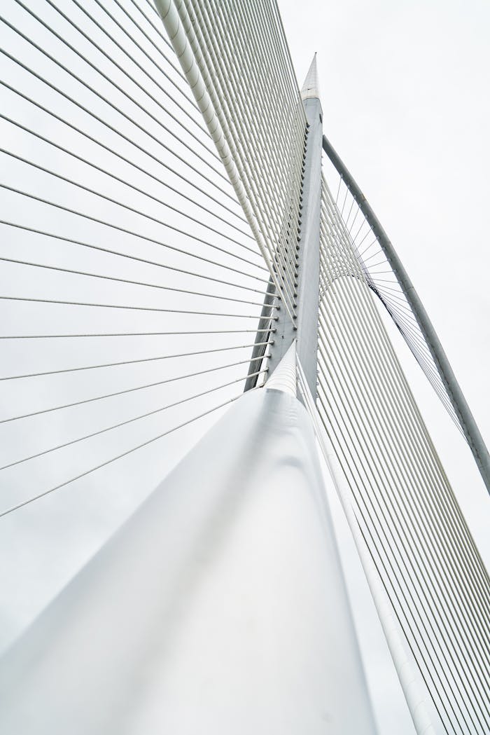 Low angle view of a modern suspension bridge with steel cables and architectural lines under a cloudy sky.